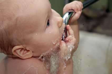 little baby drinking water from the tap during bathing